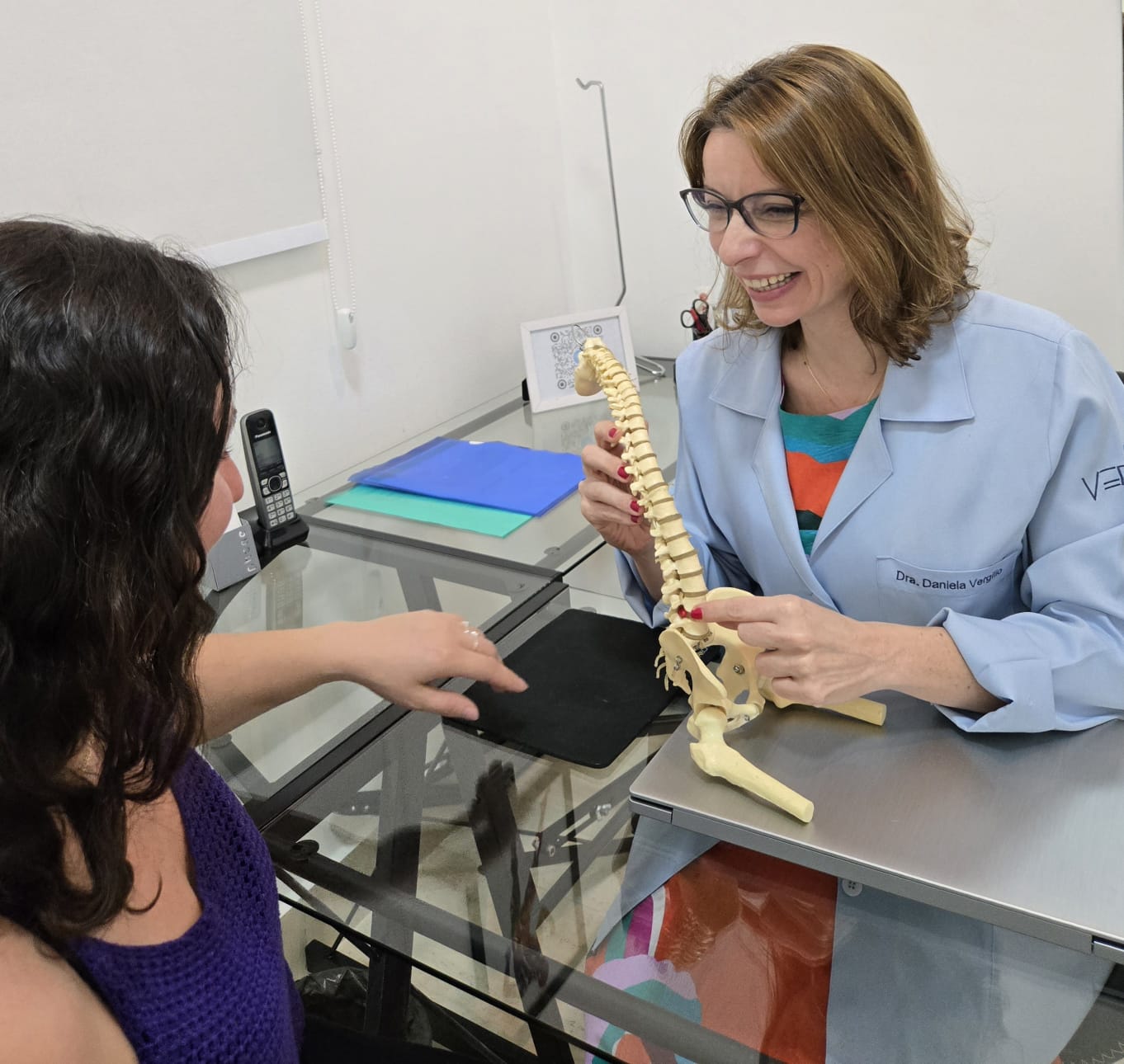 Fisioterapeuta explicando o caso ao paciente com modelo anatômico da coluna
